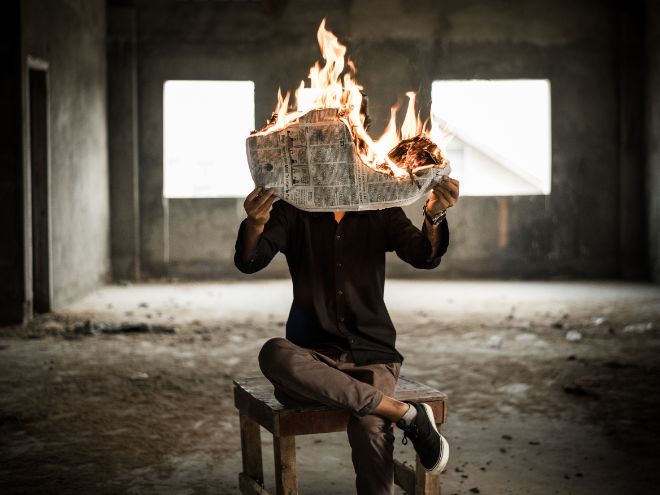 Mann sitter på en stol med en brennende avis i hendene.