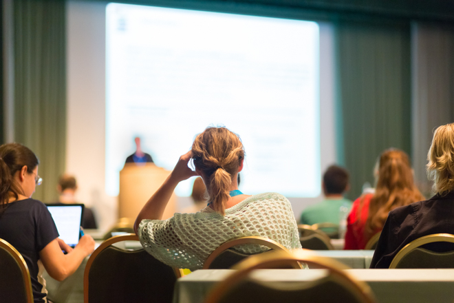 image of a woman sitting and listening to a research presentation